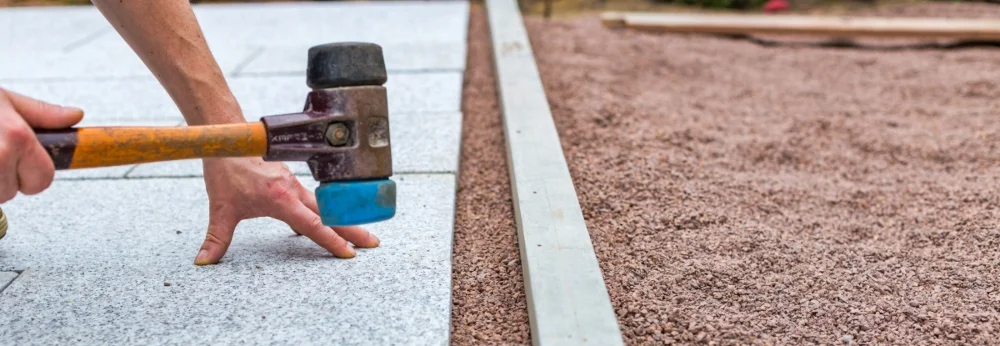 Person verlegt Steinplatte mit Gummihammer